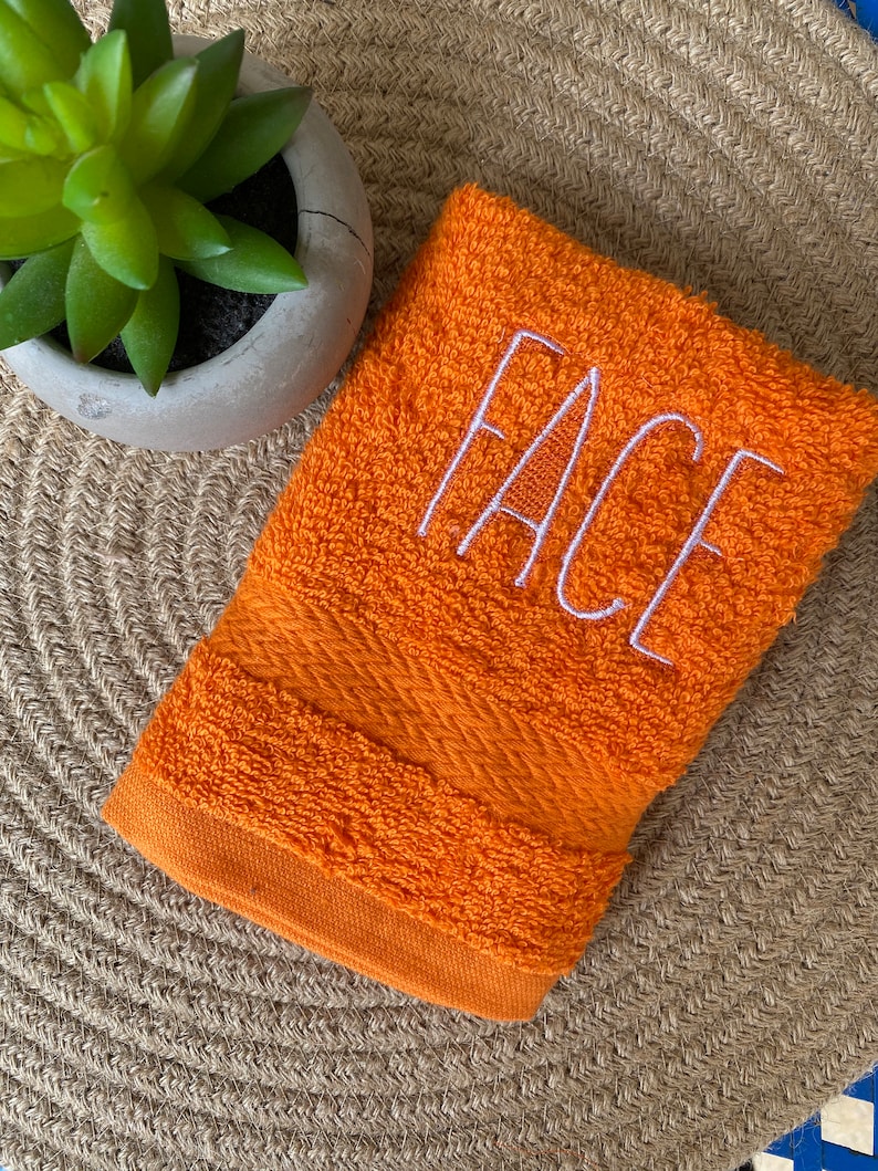 May include: Orange hand towel with the word "FACE" embroidered in white.