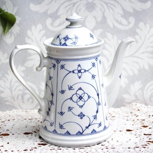 Könnte beinhalten: Eine weiße Kaffeekanne aus Keramik mit einem blauen und weißen Blumenmuster. Die Kanne hat einen Deckel und einen Henkel.