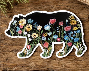 May include: A die-cut sticker shaped like a bear silhouette with a black background filled with a colorful floral pattern. The design features various painted flowers in shades of red, yellow, blue, and white, with green stems and leaves.