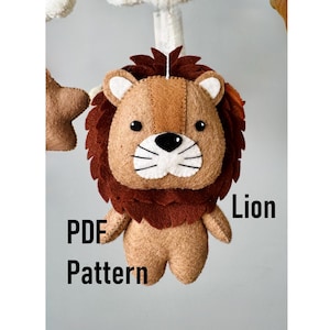 May include: A felt lion mobile with a brown mane, tan face, and white accents. The text "PDF Pattern" and "Lion" are displayed. This handmade item is likely for a nursery or baby room.