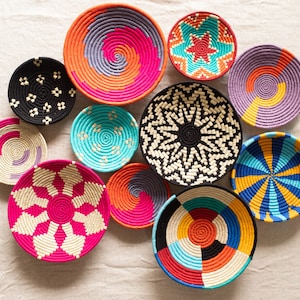 Puede incluir: Una colección de 10 cestas tejidas de colores con varios patrones geométricos y en espiral. Las cestas están hechas de materiales naturales y tienen una variedad de tamaños y formas.
