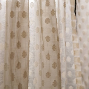 May include: Close-up of sheer white curtains with a subtle embossed pattern of brown leaves. The curtains are gathered and draped, creating a soft and airy look.