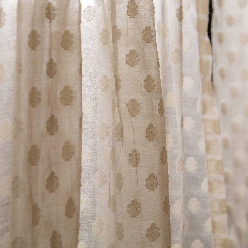 May include: Close-up of sheer white curtains with a subtle embossed pattern of brown leaves. The curtains are gathered and draped, creating a soft and airy look.