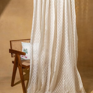 May include: White sheer curtain with a polka dot pattern. The curtain is hanging in front of a wooden chair with a patterned cushion.