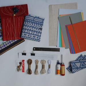 Puede incluir: Un kit de manualidades para hacer diarios y cuadernos. El kit incluye dos cubiertas de tela, una regla, un punzón de metal, una botella de pegamento, hilo, botones y una variedad de papeles de colores.