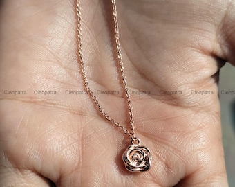 May include: Rose gold necklace featuring a delicate rose pendant. The pendant is a detailed miniature rose, suspended from a fine chain. The necklace is displayed on a hand, showcasing the jewelry's design and color.