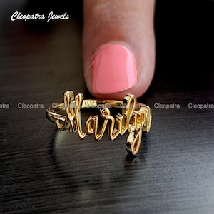 Könnte beinhalten: Goldfarbener Ring mit dem Namen "Marilyn" in Schreibschrift.