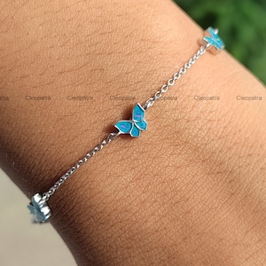 May include: A silver bracelet featuring a delicate chain and three butterfly charms. The butterfly charms are a vibrant turquoise color with a detailed design. The bracelet is a stylish piece of jewelry.