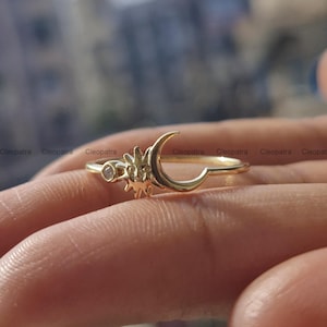 May include: Gold ring with a crescent moon and sun design, featuring a small clear gemstone.