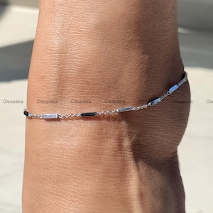 May include: A silver ankle bracelet with a delicate chain and small rectangular charms.
