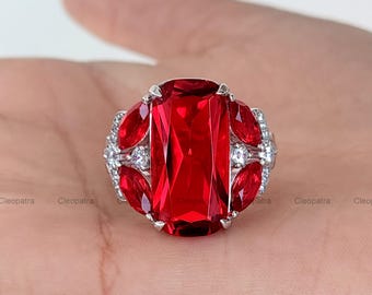 May include: A silver ring featuring a large, rectangular, faceted red gemstone as the centerpiece. The ring is accented with smaller, marquise-cut red stones and clear, round accent stones.