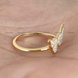 May include: A gold ring with a leaf-like design encrusted with small, sparkling stones. The ring is set against a neutral background, highlighting its intricate details and craftsmanship. The ring is marked with "10K" and the name "Cleopatra".