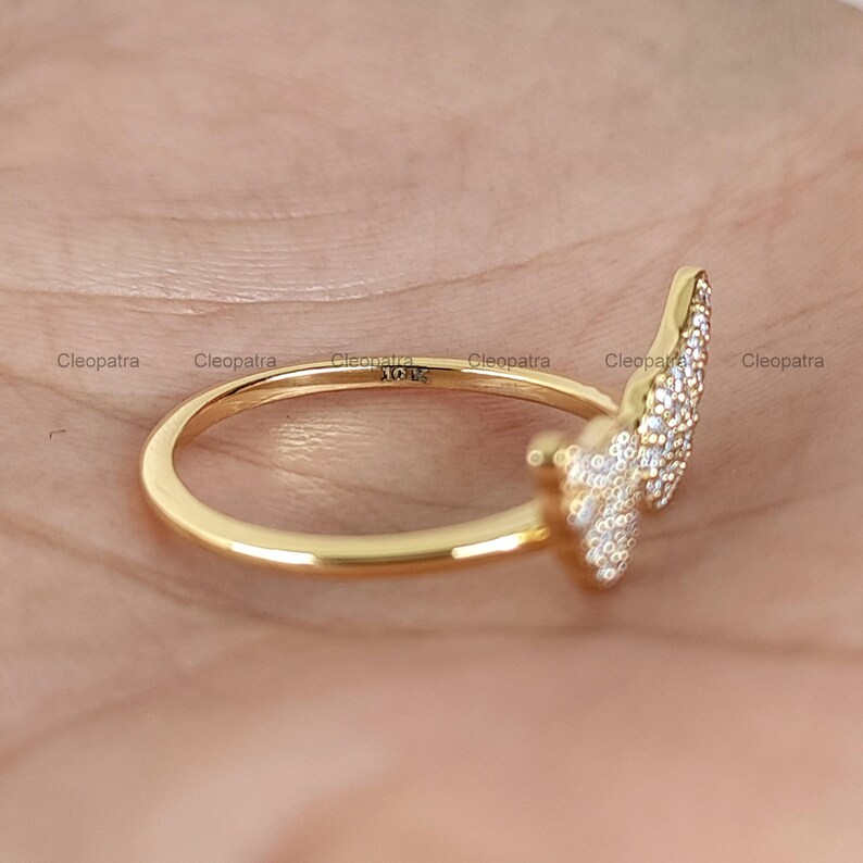 May include: A gold ring with a leaf-like design encrusted with small, sparkling stones. The ring is set against a neutral background, highlighting its intricate details and craftsmanship. The ring is marked with "10K" and the name "Cleopatra".