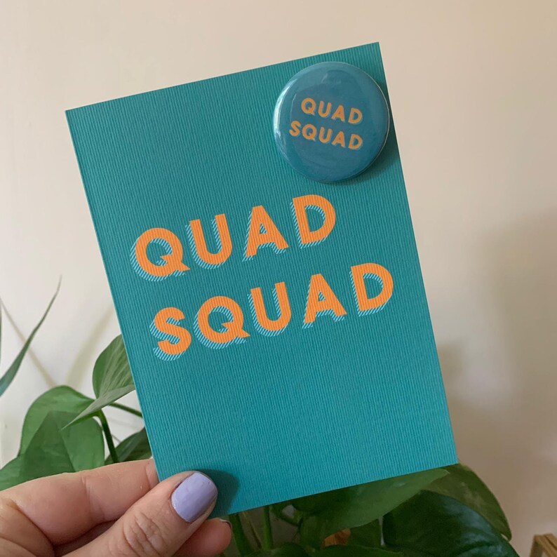 May include: Teal card with the text "QUAD SQUAD" in orange letters. A teal button with the text "QUAD SQUAD" in orange letters is attached to the top of the card.