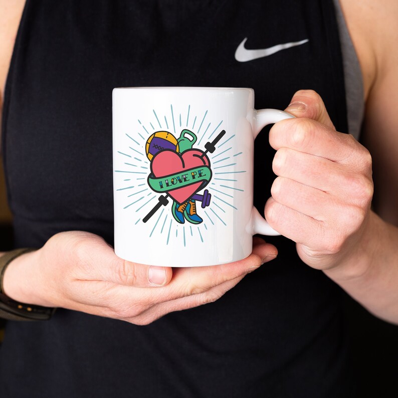 May include: White ceramic coffee mug with a colorful graphic of a heart with a banner that says "I LOVE PE" and various sports equipment, including a basketball, dumbbell, and running shoes.