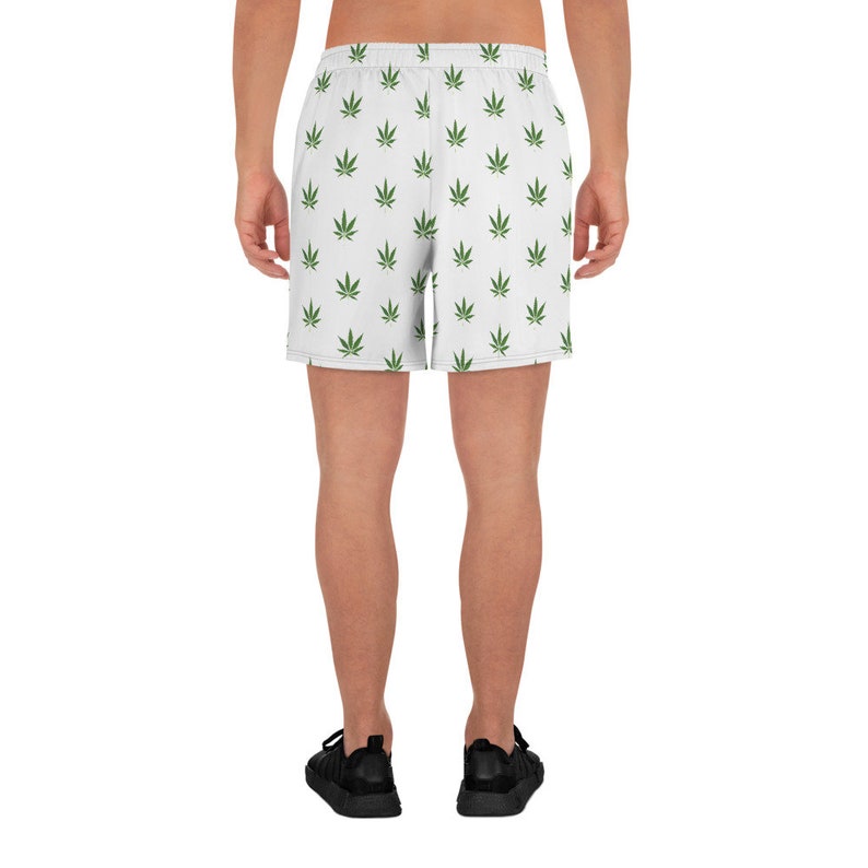 May include: White athletic shorts with a green marijuana leaf pattern. The shorts have an elastic waistband and a drawstring.