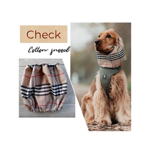May include: A beige and black plaid cotton snood for dogs. The snood is worn by a brown and white dog with a green harness. The text "Check Cotton Snood" is visible in the image.