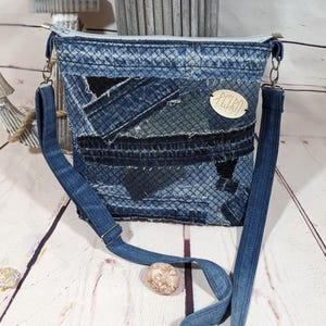 Könnte beinhalten: Eine Patchwork-Umhängetasche aus Denim mit einem blauen Denim-Riemen und silberfarbener Hardware. Die Tasche hat eine Vielzahl von Denim-Patches in verschiedenen Blautönen. Ein kleines, ovales Etikett mit dem Wort "PELURA" ist angebracht.
