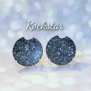 May include: Two round black glitter coasters with the word "Rockstar" printed above them. The coasters are on small clear stands.