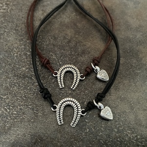 May include: Two leather bracelets with silver charms. One charm is a horseshoe and the other is a heart.