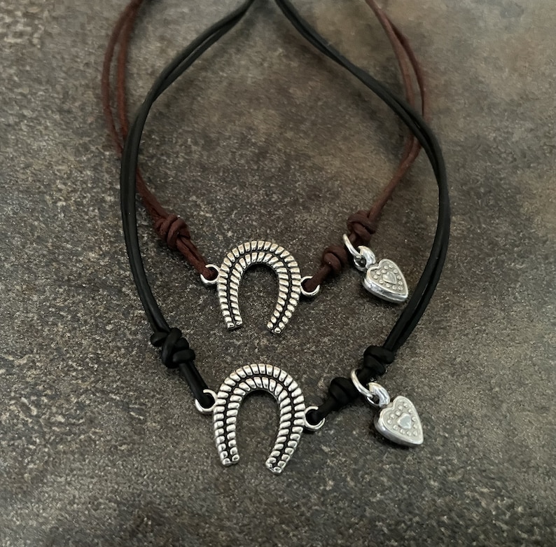 May include: Two leather bracelets with silver charms. One charm is a horseshoe and the other is a heart.
