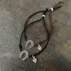 May include: Two leather bracelets with silver charms. One charm is a horseshoe and the other is a heart.