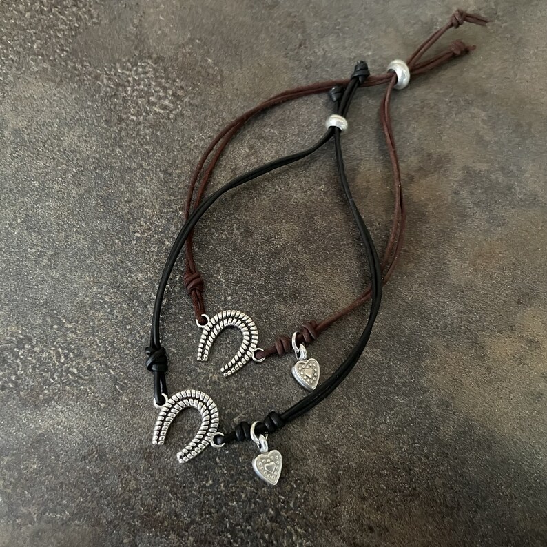 May include: Two leather bracelets with silver charms. One charm is a horseshoe and the other is a heart.