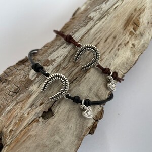 May include: Two leather bracelets with silver horseshoe charms and heart charms. One bracelet is brown leather and the other is black leather.