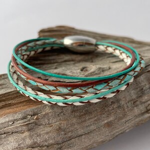 May include: A multi-strand leather bracelet with a magnetic clasp. The bracelet is made of white, brown, and turquoise leather.