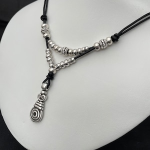 Peut inclure: Un collier en argent avec un pendentif au design stylisé. Le collier est fait d'un cordon en cuir noir et de perles en argent.