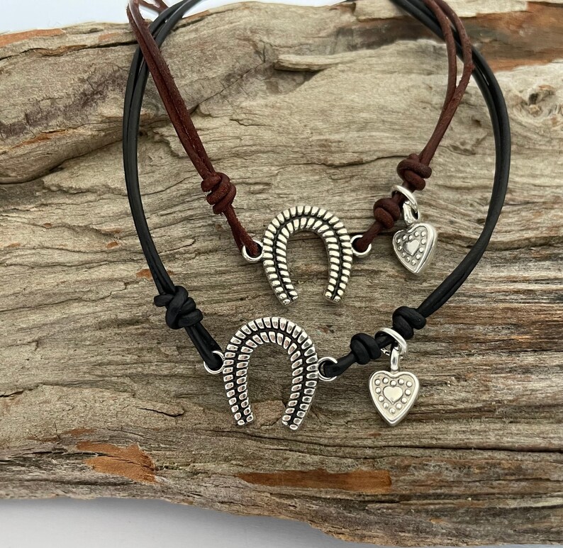 May include: Two leather bracelets with silver charms. One bracelet is black and the other is brown. The charms are a horseshoe and a heart.