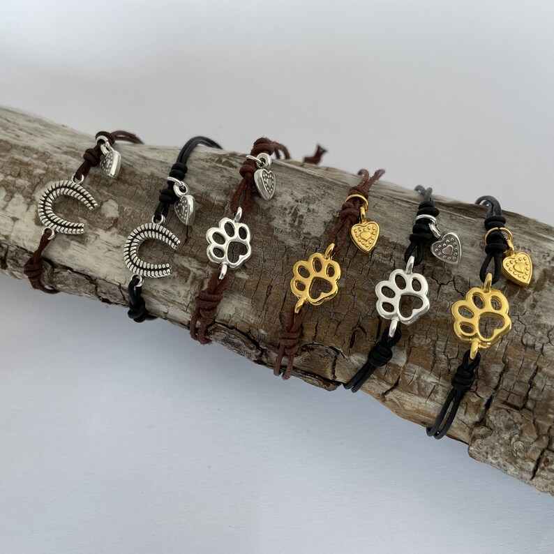 May include: Six leather bracelets with silver and gold charms. The charms include paw prints, hearts, and horseshoes. The bracelets are brown and black.
