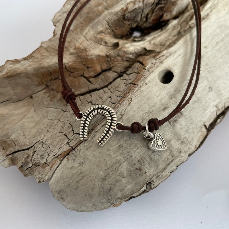 May include: A brown leather bracelet with a silver horseshoe charm and a small silver heart charm.