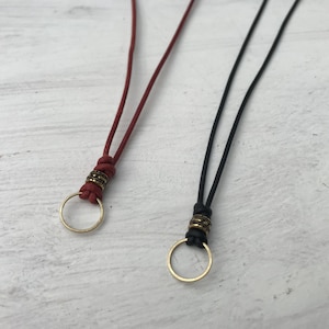 Puede incluir: Dos collares de cordón de cuero con un anillo de latón en el extremo. Uno es rojo y el otro es negro.