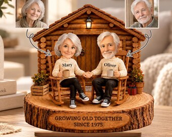 May include: A 2D flat ornament featuring two figurines of an older couple sitting in rocking chairs in front of a log cabin. The figurines wear cream sweaters labeled Mary and Oliver. The base is wood-textured with the text GROWING OLD TOGETHER SINCE 1975.