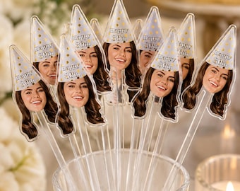 May include: A collection of clear plastic cake toppers featuring a cutout of a smiling face wearing a white party hat with gold polka dots and the text Happy 30th. Each topper is attached to a long, transparent stick for insertion into food.