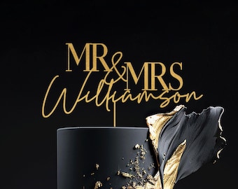 May include: A two-tiered black wedding cake with gold accents and a gold "MR & MRS Williamson" cake topper. The cake is decorated with gold leaf and abstract black and gold shapes.