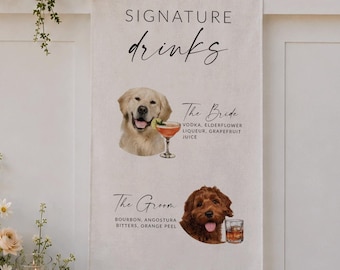 May include: A white bar counter featuring a sign that reads SIGNATURE drinks with illustrations of two dogs and cocktail descriptions. A large floral arrangement with white and blush flowers sits on top, alongside glass bottles and a framed menu.