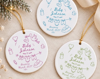 May include: Three round white ceramic ornaments with gold hanging strings. Each features a line art illustration of a stork, baby items, and the text Baby Johnson Arriving March 2027. One ornament has blue ink, one purple, and one green.