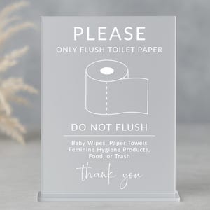 Pode incluir: Um sinal branco com texto cinza que diz "PLEASE ONLY FLUSH TOILET PAPER" com uma ilustração branca de um rolo de papel higiênico. O sinal também diz "DO NOT FLUSH" e lista os itens que não devem ser descartados no vaso sanitário, incluindo "Baby Wipes, Paper Towels, Feminine Hygiene Products, Food, or Trash". O sinal termina com "thank you".