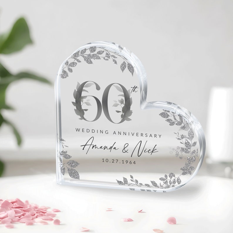 May include: A clear heart-shaped acrylic paperweight with a silver glitter design. The paperweight features the text "60th Wedding Anniversary Amanda & Nick 10.27.1964".
