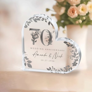 May include: A clear heart-shaped acrylic paperweight with a floral design and the text "70th Wedding Anniversary Amanda & Nick 10.27.1954"