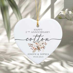 Peut inclure: Ornement en c&eacute;ramique blanche en forme de c&oelig;ur avec une ficelle dor&eacute;e pour l'accrocher. L'ornement pr&eacute;sente un motif floral avec des boules de coton et le texte "Happy 2nd Anniversary Cotton Joseph & Sophia 09.16.2024".