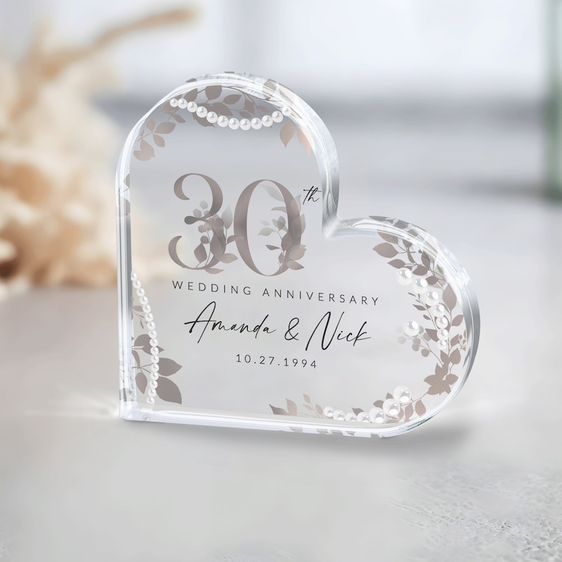 May include: A clear heart-shaped crystal paperweight with a 30th wedding anniversary design. The design features a floral pattern with pearl accents and the text "30th Wedding Anniversary Amanda & Nick 10.27.1994".