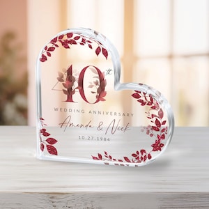 May include: A clear heart-shaped crystal paperweight with a red glitter design. The number 40 with a superscript "th" is in the center of the heart. The text "Wedding Anniversary" is below the number, followed by the names "Amanda & Nick" and the date "10.27.1984".