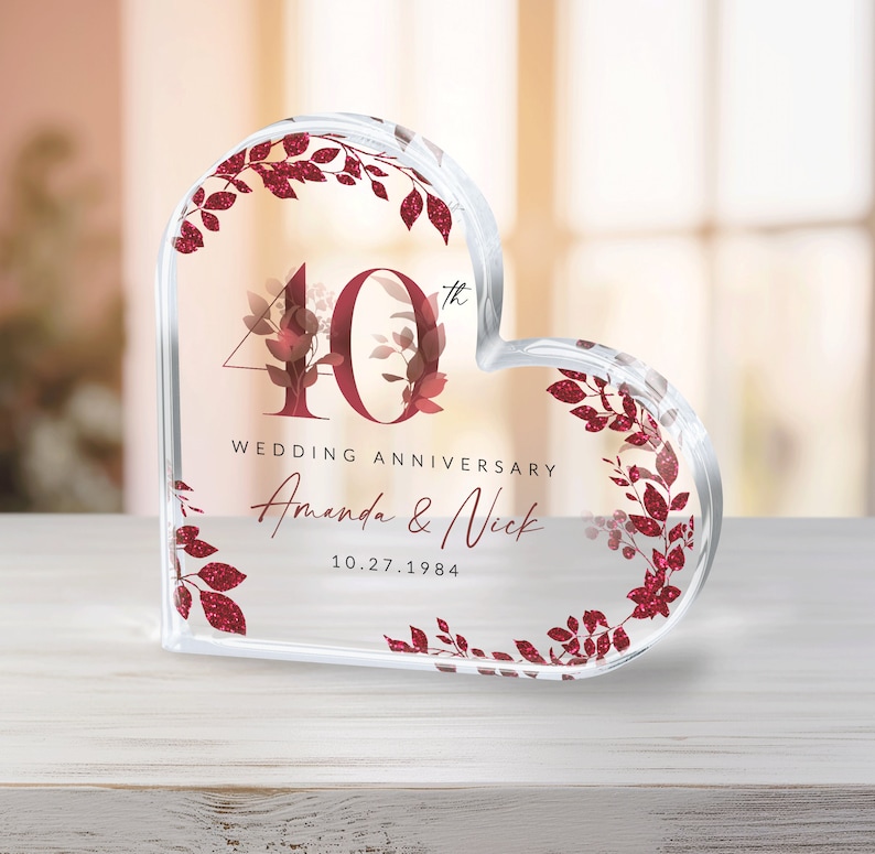 May include: A clear heart-shaped crystal paperweight with a red glitter design. The number 40 with a superscript "th" is in the center of the heart. The text "Wedding Anniversary" is below the number, followed by the names "Amanda & Nick" and the date "10.27.1984".