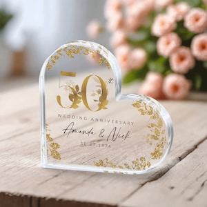 May include: A clear heart-shaped acrylic paperweight with gold glitter and floral accents. The number 50th is displayed in gold with the text "Wedding Anniversary Amanda & Nick 10.27.1974".