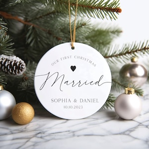 May include: White round Christmas bauble with the text "Our First Christmas Married" and a small black heart. Below the text is "Sophia & Daniel 10.10.2023".