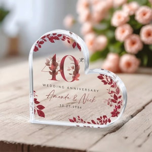 May include: A clear heart-shaped acrylic paperweight with a red glitter design. The paperweight features the number 40 with a floral design and the text "Wedding Anniversary Amanda & Nick 10.27.1984".