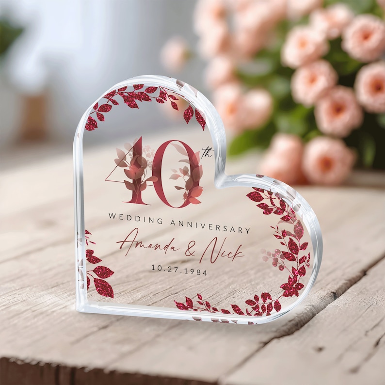 May include: A clear heart-shaped acrylic paperweight with a red glitter design. The paperweight features the number 40 with a floral design and the text "Wedding Anniversary Amanda & Nick 10.27.1984".